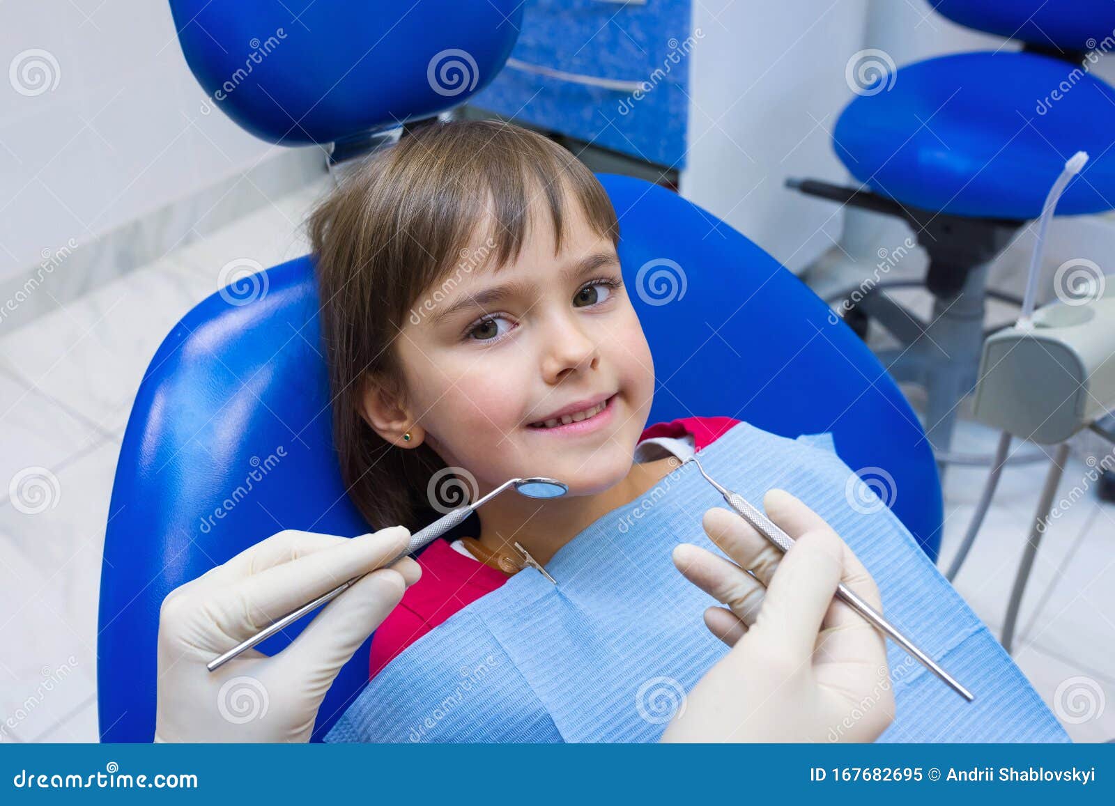 a lovely little girl sitting in a dental chair in hospital. a child dentistÃ¢â¬â¢s hands. a little girl sitting at the dentistÃ¢â¬â¢s